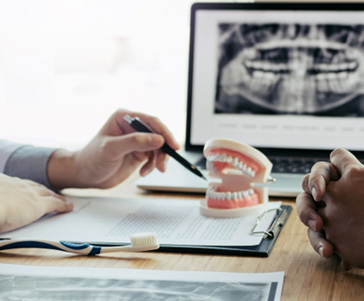 Hands of dentist and patient discussing model teeth and X-rays at desk