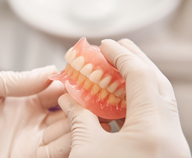 Close-up of full dentures held by gloved hands