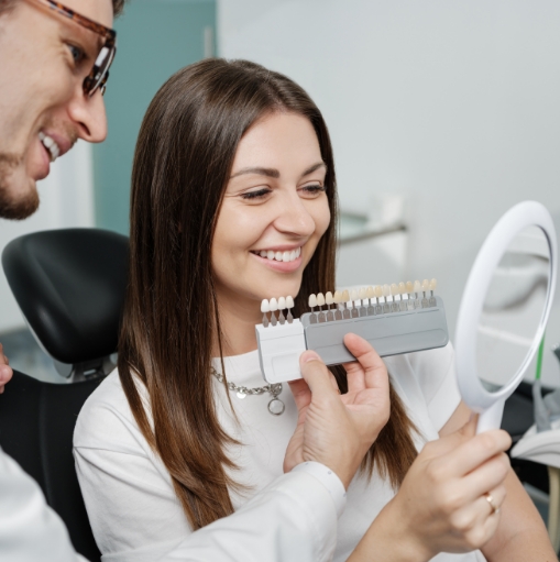 Dentist holding a row of veneers in front of a patient's smile